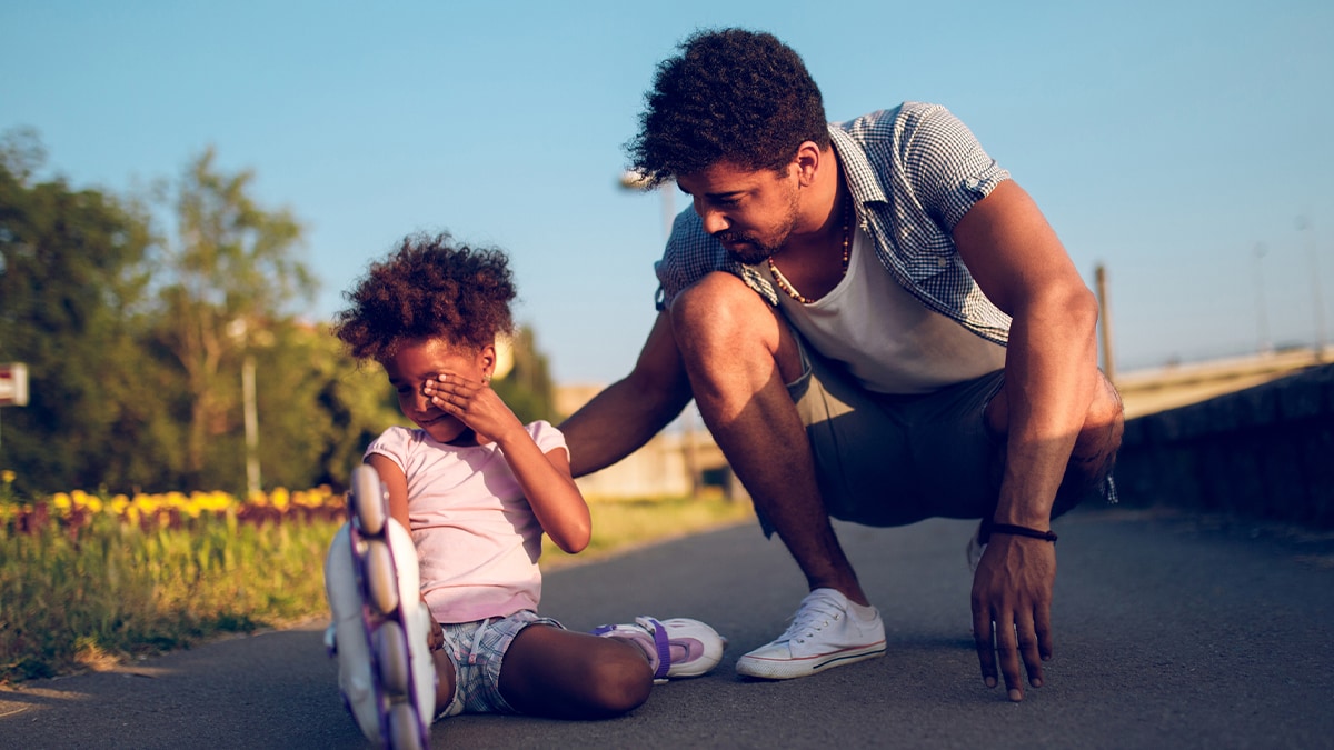 A father is comforting his daughter who just fell rollerblading