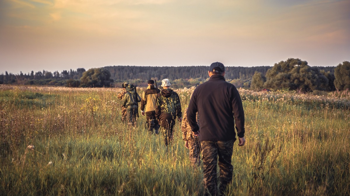 Hunters walking in tall grass.