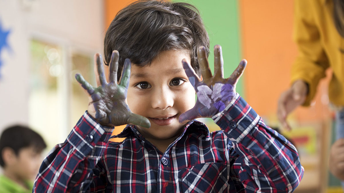 Young boy smiling while holding up hands after finger painting