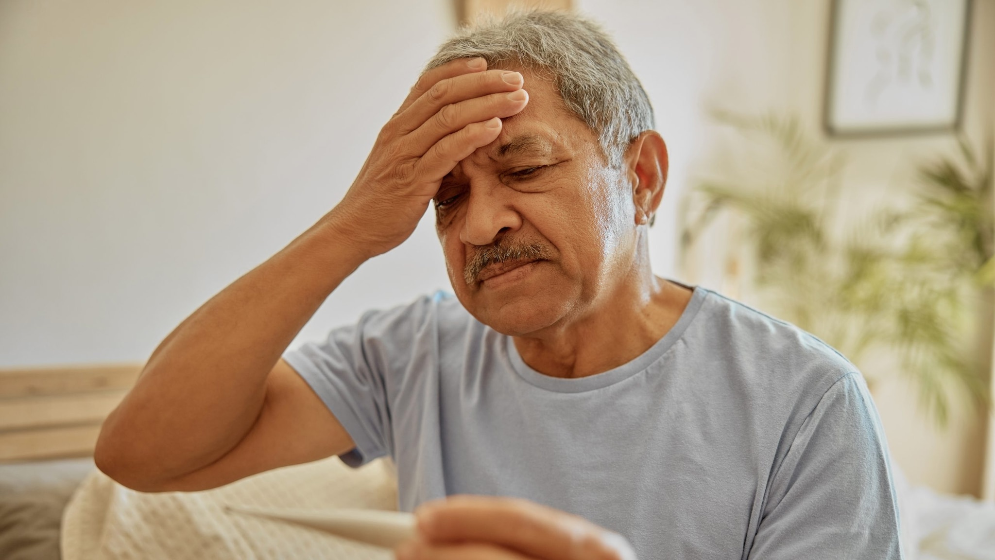 Man feeling his head with one hand and reading a thermometer in the other.