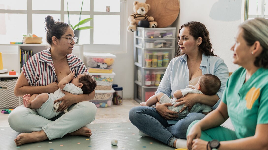 A group of moms sit on the floor and breastfeed their babies.