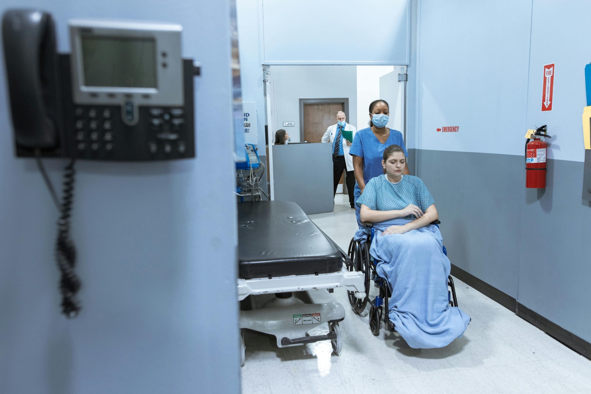 Healthcare personnel pushing patient in wheelchair.