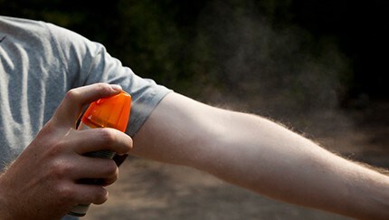 A man is spraying bug spray on his arm.