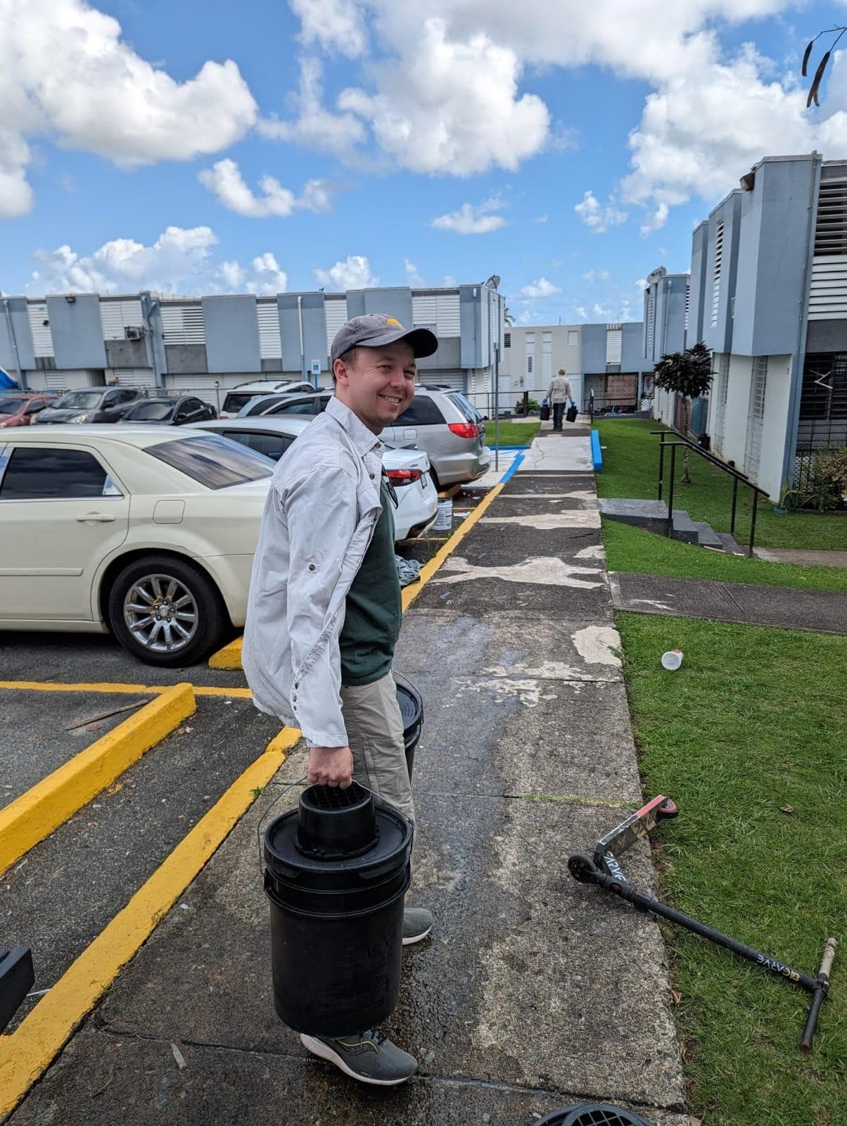 A person outside in an apartment complex looking back at the camera and smiling while carrying AGO traps.