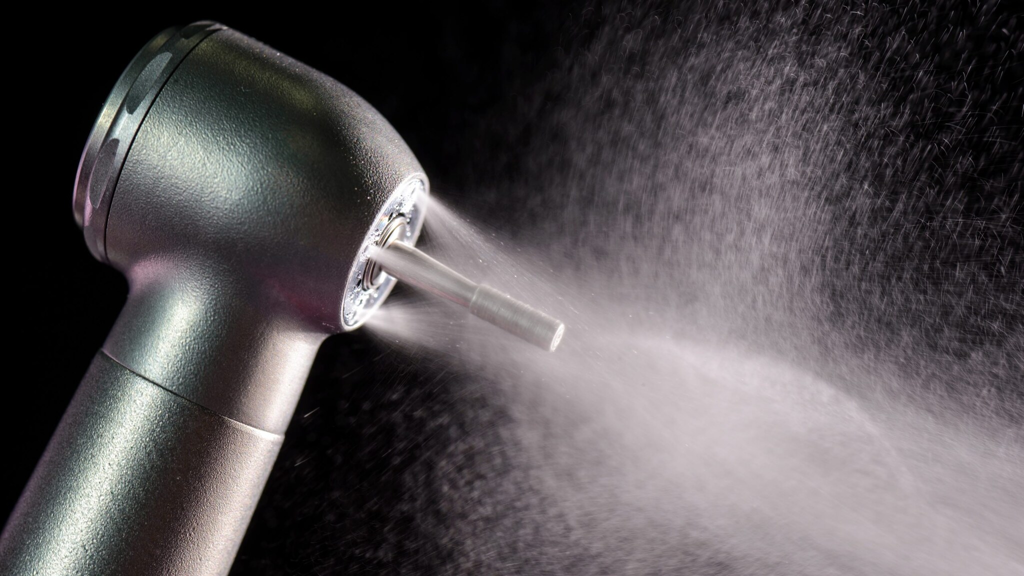 Black background with a silver dental handpiece spraying water.