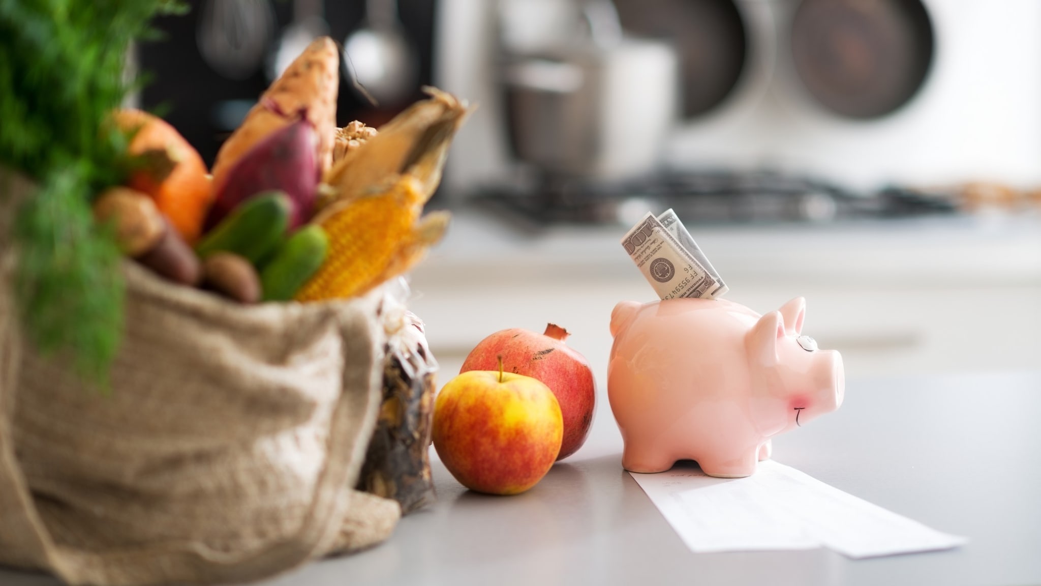 Dinero dentro de una alcancía y una compra de alimentos sobre una mesa.