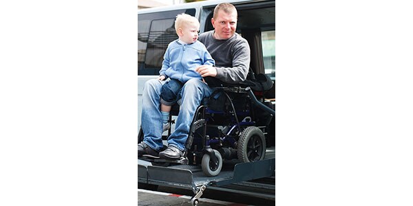 A man is using a wheelchair and holding a child on his lap.