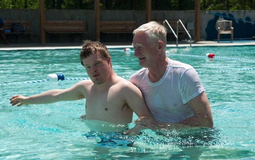 A man helps a boy with Down Syndrome in a pool.