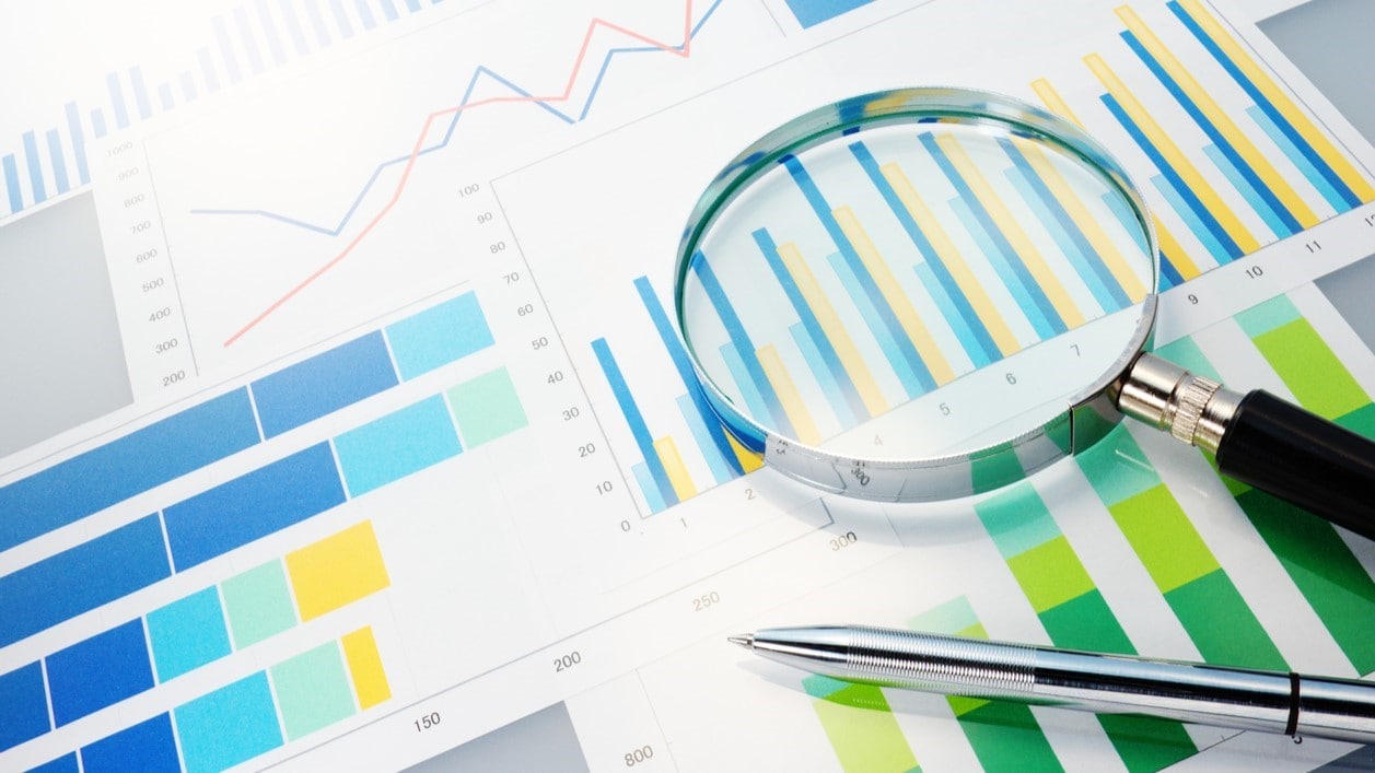 Magnifying glass and pen on paper printed with colorful bar charts.