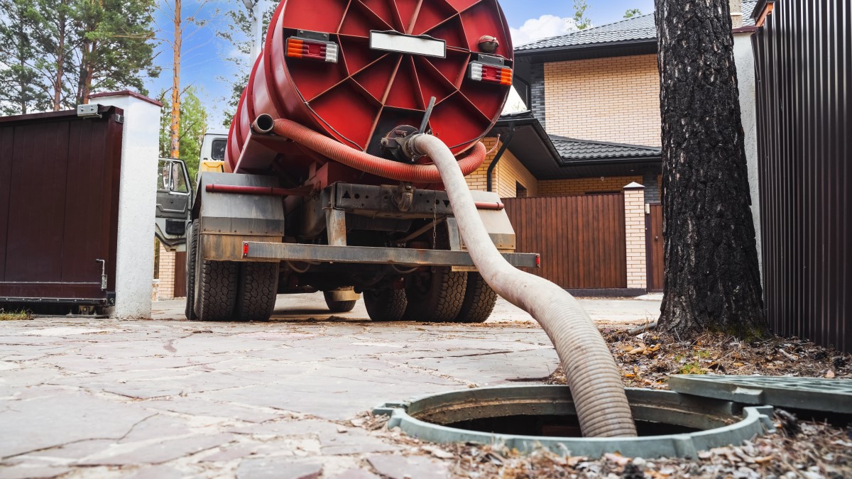 Large truck with a pipe extending out of its holding tank into a septic system access opening in the ground