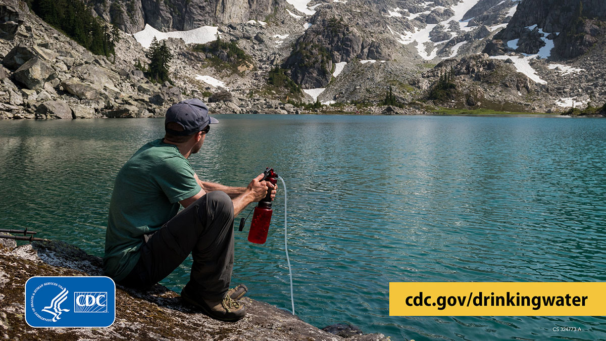 Hiker sitting next to a clear mountain lake and using a filter to treat water from the lake.