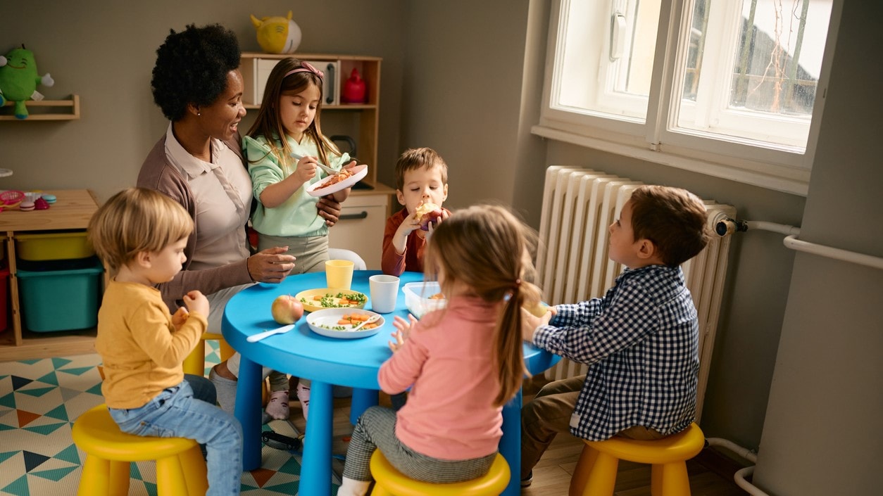 Teacher and young children sitting at a table eating nutritious foods.