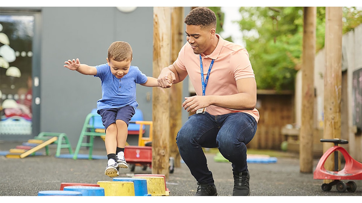 An early educator helping a child jump on the playground.