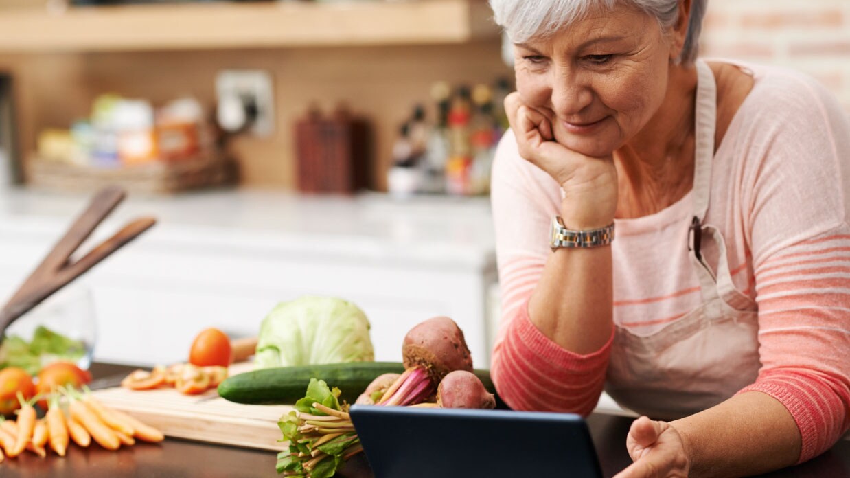 A woman reading recipe on tablet while preparing vegetables.