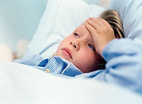 Young boy laying down with his hand over his forehead.