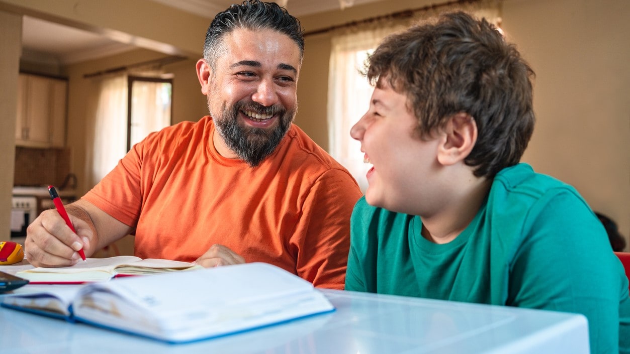 Father and son at a table with an open notebook.