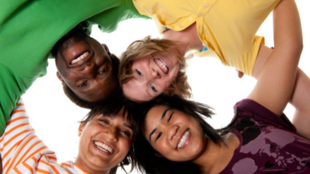 Four teens with arms connected and head together huddled looking down at camera