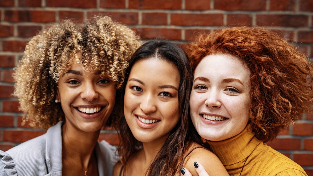 Three women standing closely together and smiling