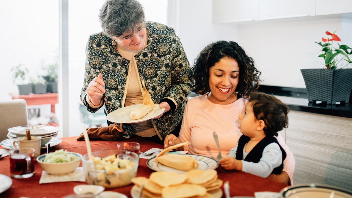 A family sitting at a table with tortillas and tamales on their plates.