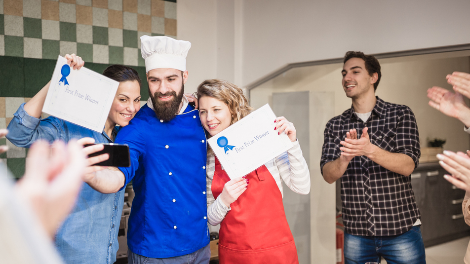 Cropped recognition programs Chef and kitchen staff taking a selfie after receiving recognition with audience applauding.