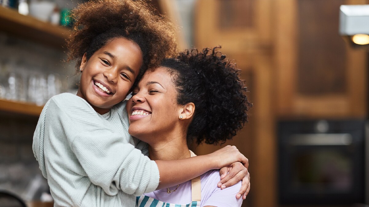 Niña abrazando a su madre, sonriendo.