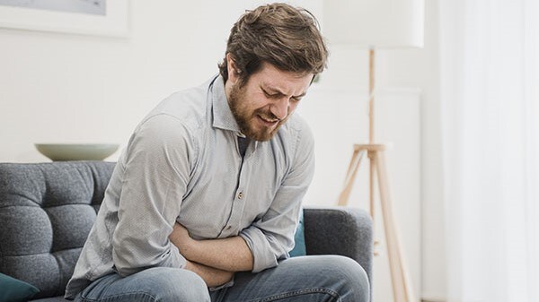 Man sitting on a couch holding his stomach in pain