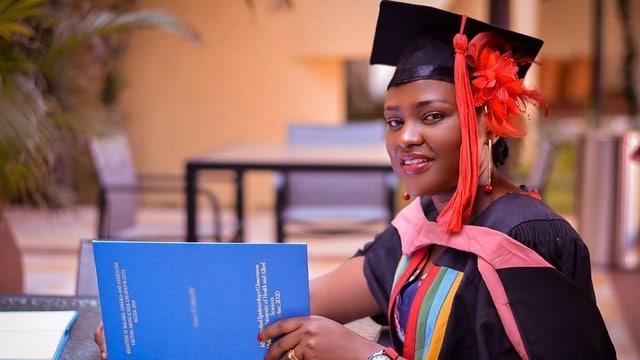 Woman with graduation attire sitting at a table with a book open.