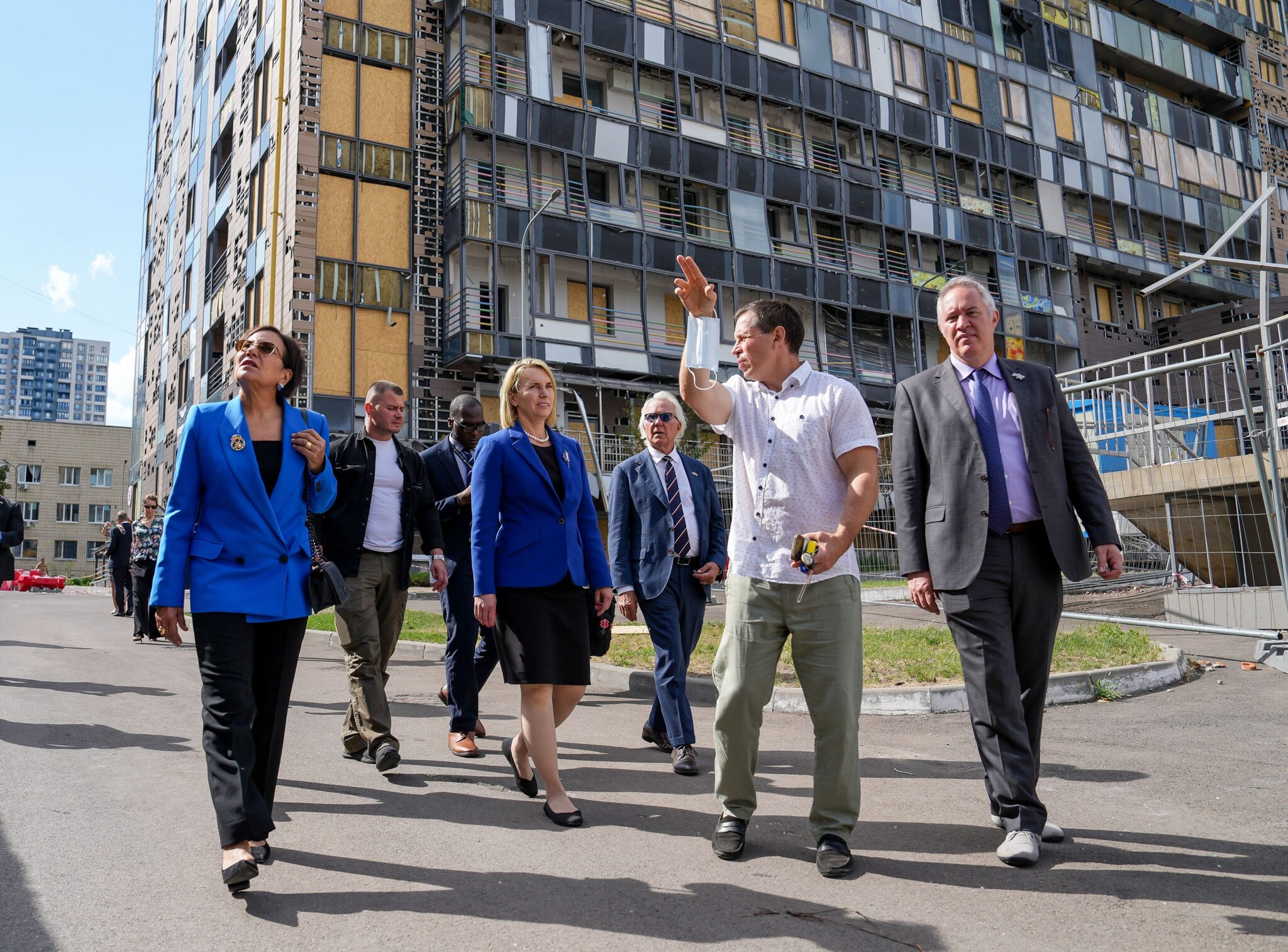 A group of officials walking outdoors near a damaged building.