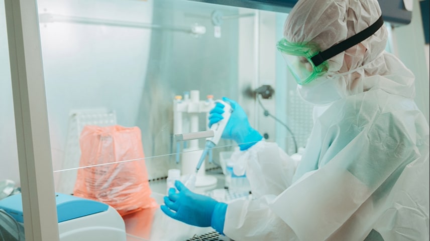 Photo of laboratorian wearing personal protective equipment with hands inside a biological safety cabinet, holding a pipette and container. Photo by Maxim Malov.