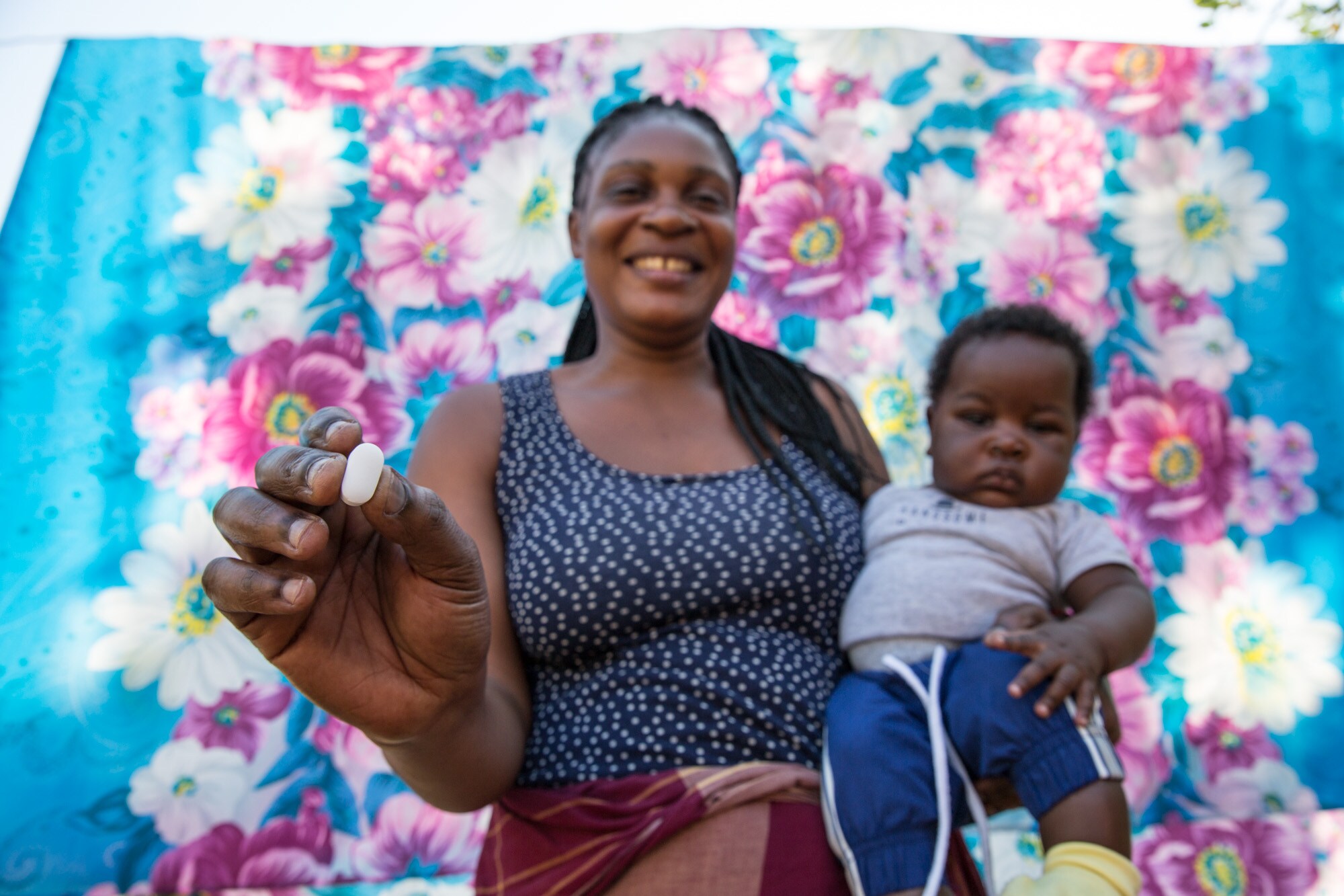 A woman with a child on her hip smiles at the camera while holding medication.