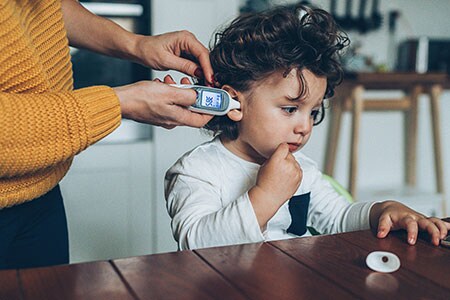 Mother takes child's temperature using a digital thermometer.