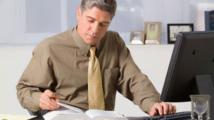 Man looking at a book while typing on a keyboard.