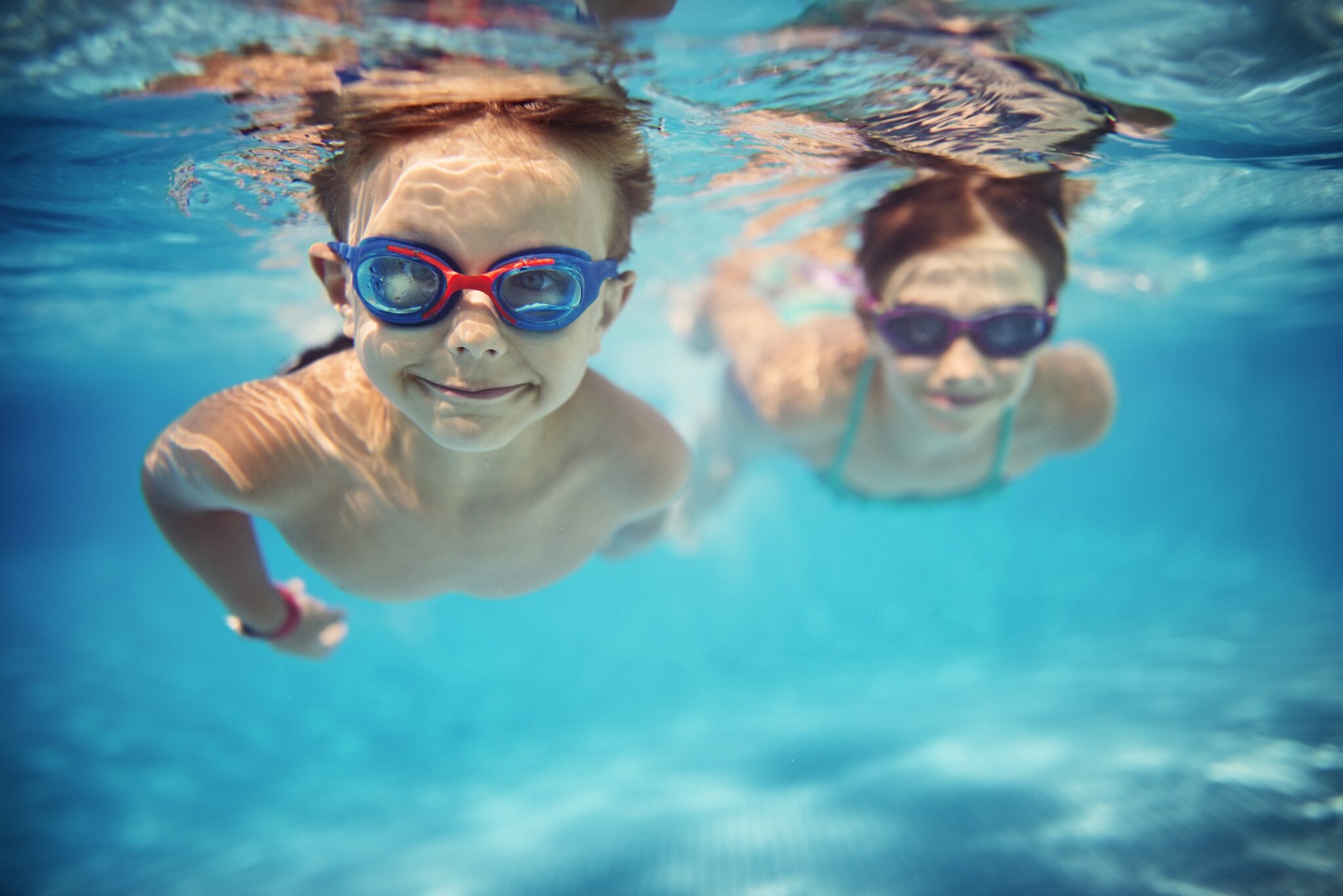 Two youn.g boys swimming in a pool under water wearing goggles