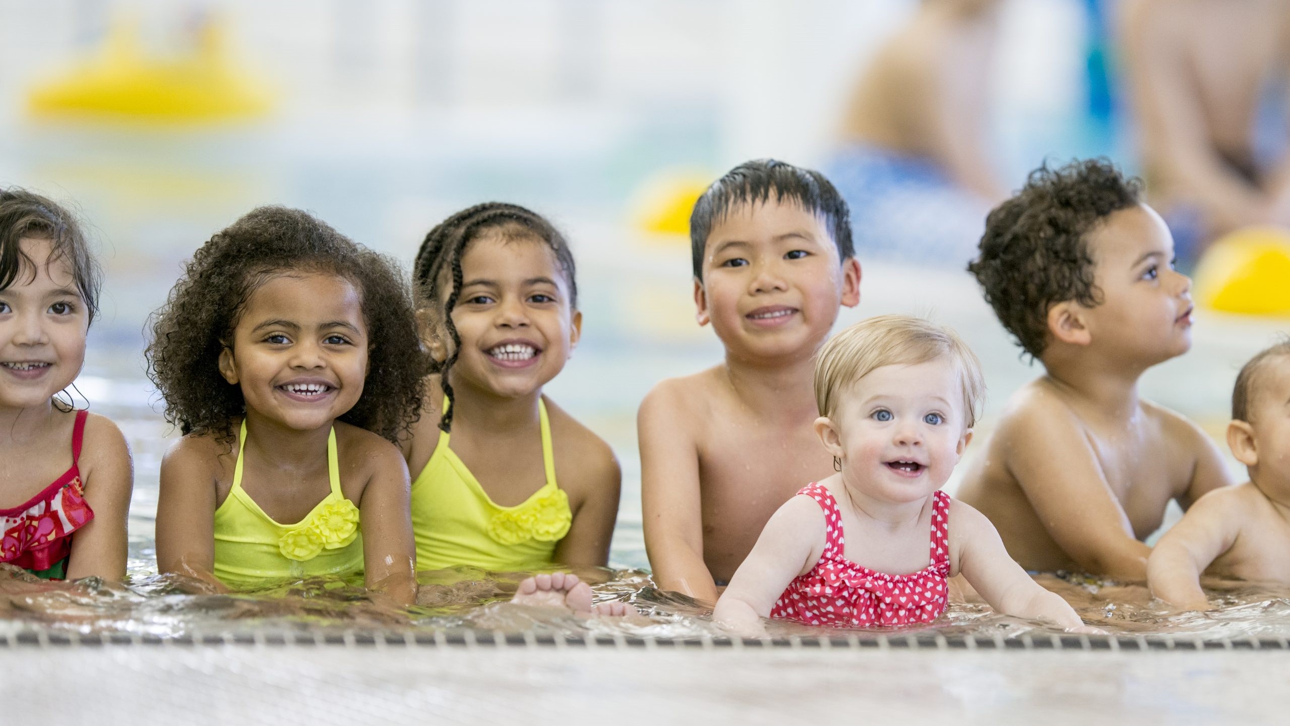 Young kids sitting in the shallow end of the pool together.