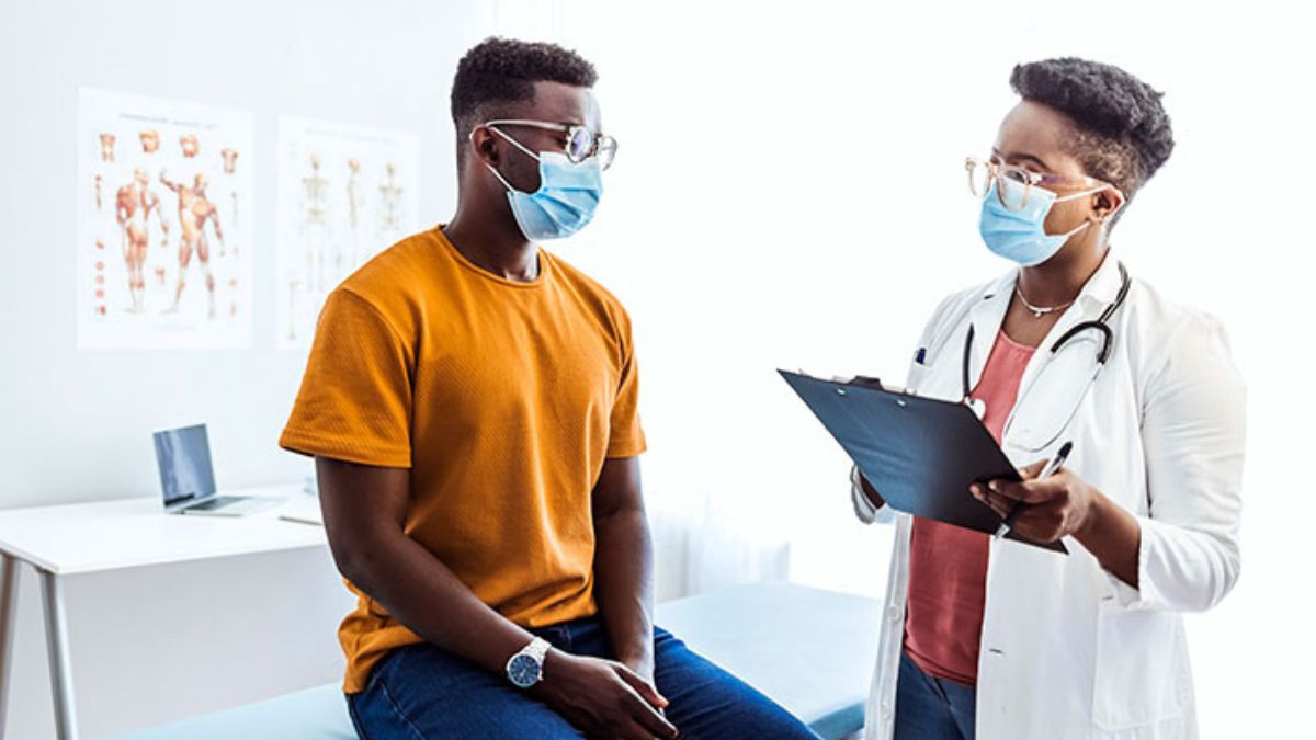 Doctor talking with male patient. Both wearing masks.