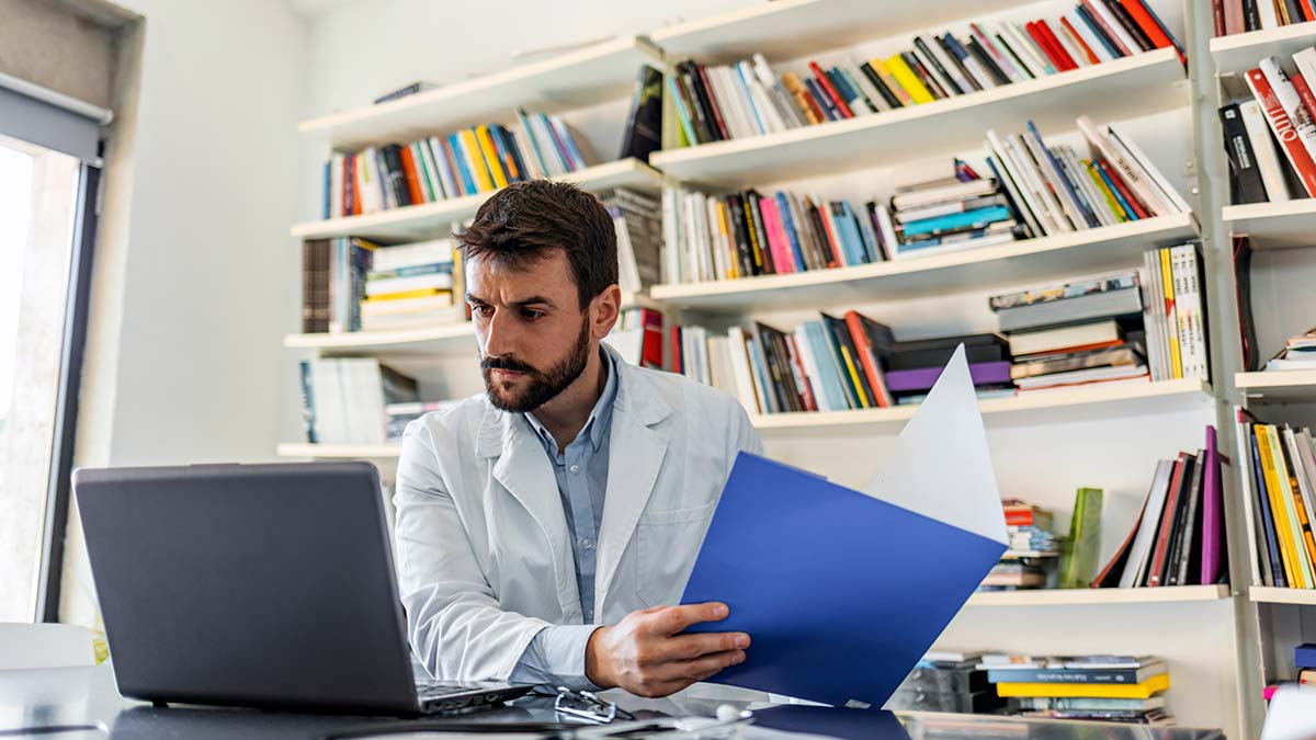 Doctor holding medical charts while reviewing hepatitis c screening recommendations on their computer