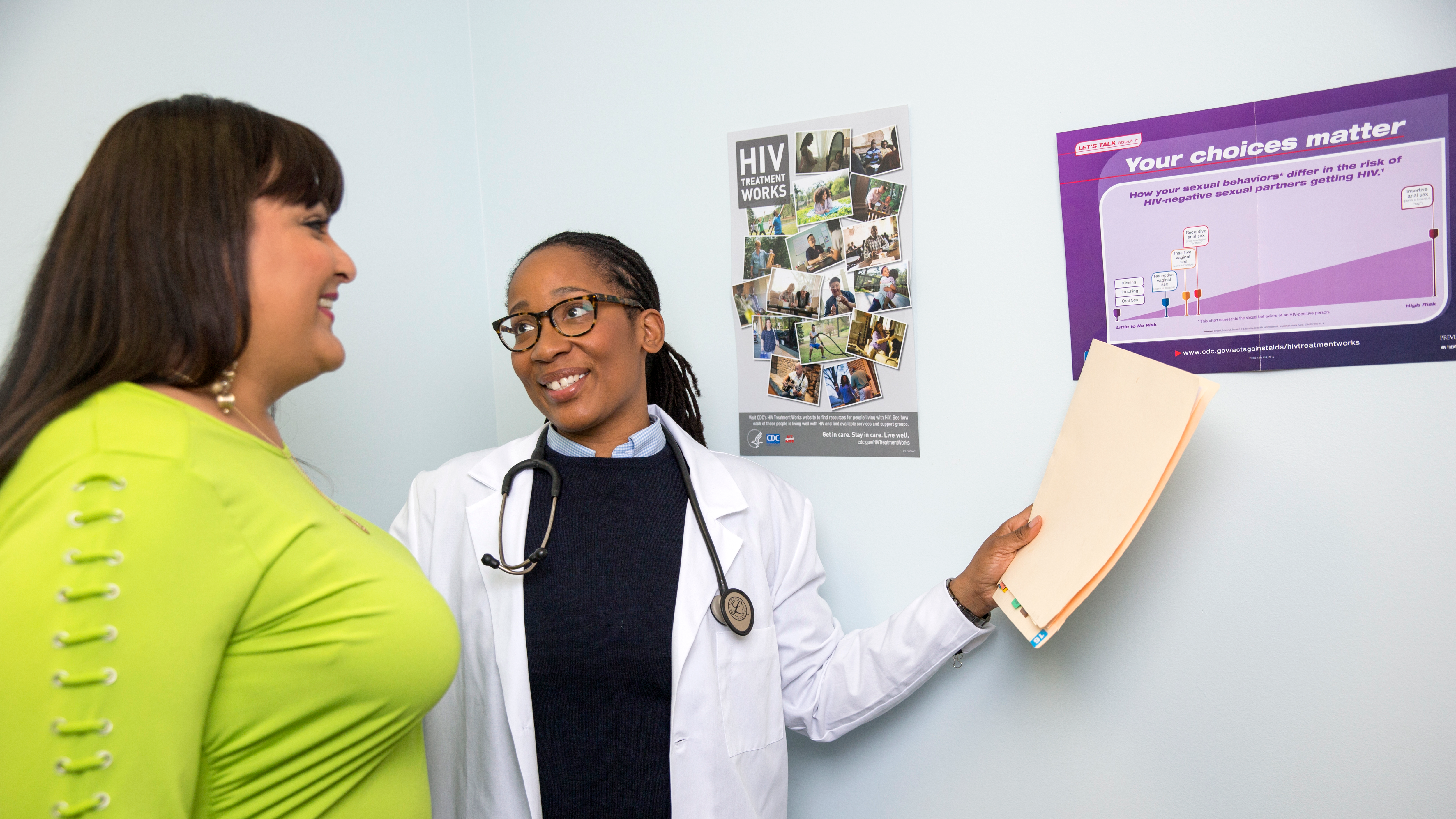 A health care provider talking to a patient points to wall posters with information about HIV.