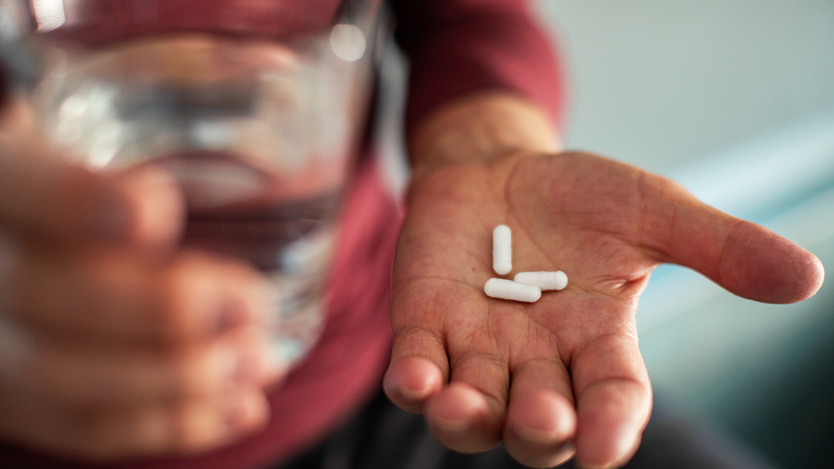 TasP Thumbnail Image of a person holding a handful of mediation (pills) with a glass of water in the other hand.