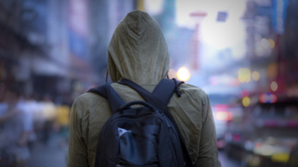 homelessness A view of the back of person wearing a backpack and a hooded sweatshirt outside in a cold busy urban setting.