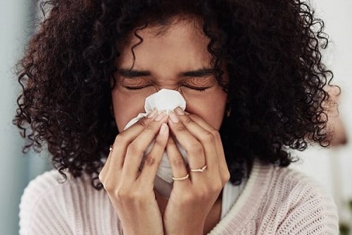 woman covering her mouth and nose with a tissue while sneezing