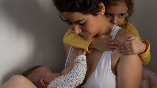 Mom breastfeeding her baby while caring for her older child.