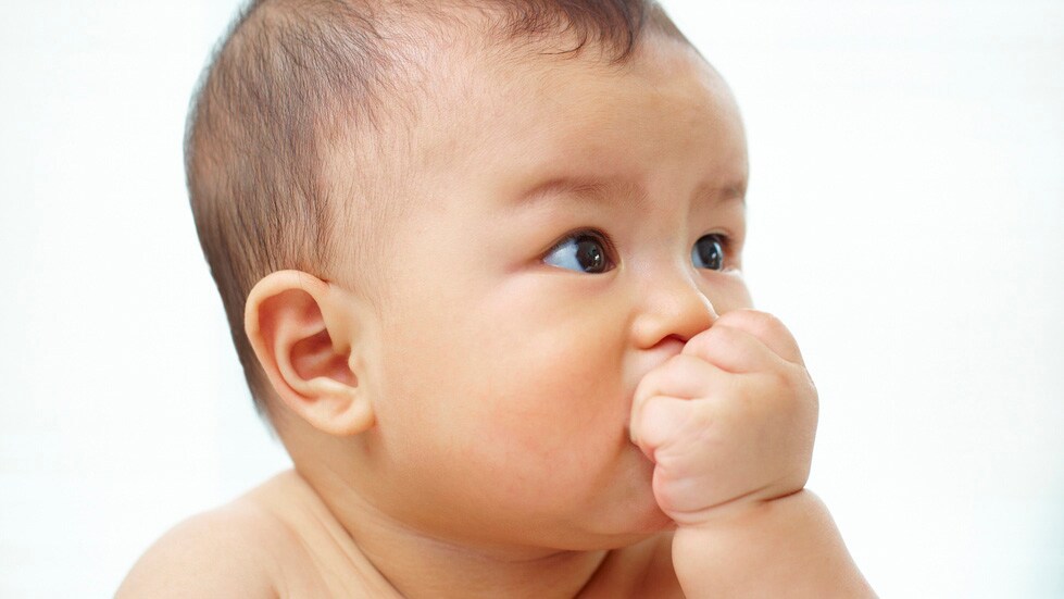 An infant putting their hand to their mouth.