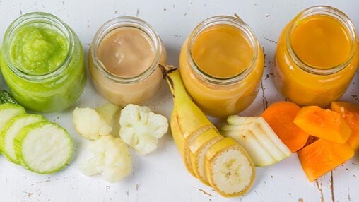 Assorted fruits and vegetables cut up into chunks, placed by small jars containing pureed versions of the same food.