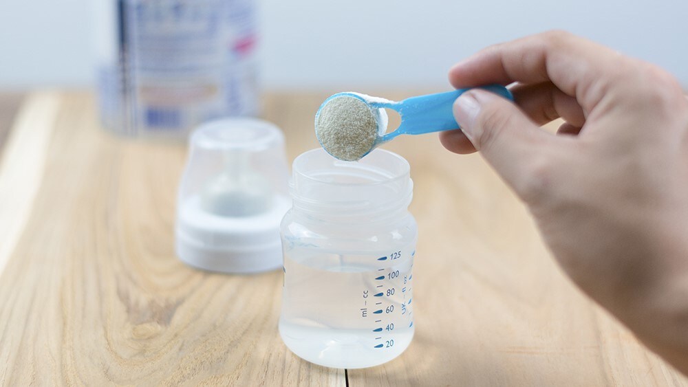 A person preparing infant formula in a bottle.