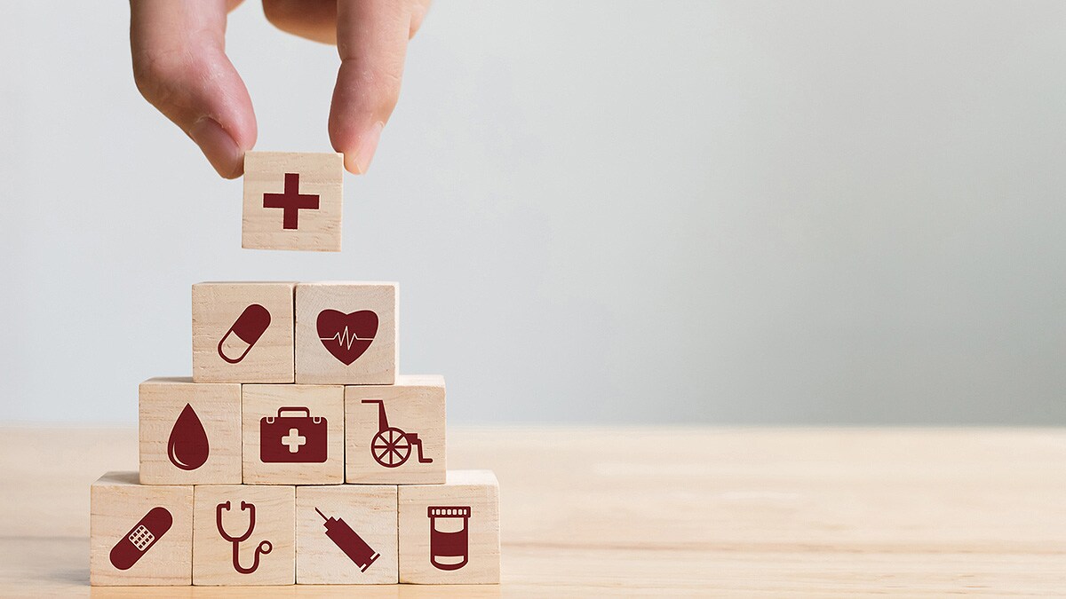 Hand placing a final wooden block on top of a pyramid of blocks, each with a different medical symbol on it.