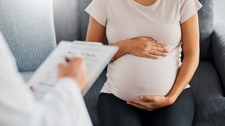 Pregnant woman in doctor's office holding her belly.