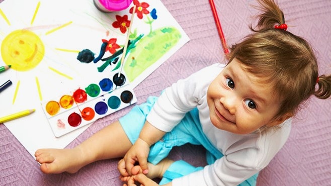 Girl looking at camera playing with a paint set.