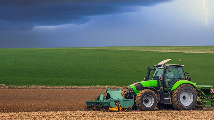 Tractor working through an empty field while there are stormy clouds and lightning in the sky.