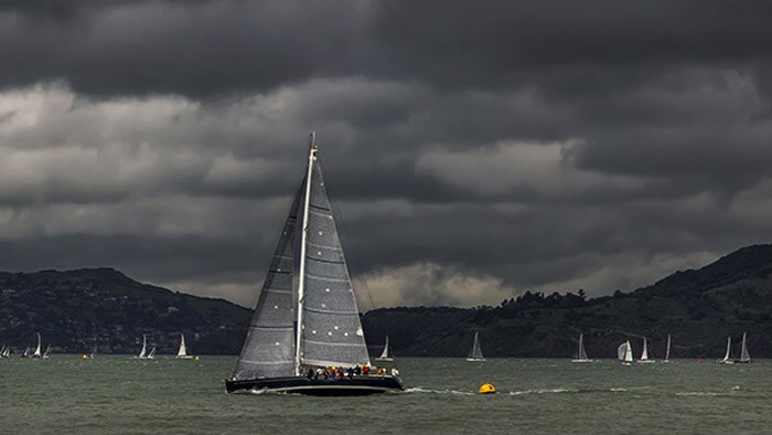 Boat sailing in the water with dark clouds looming overhead.