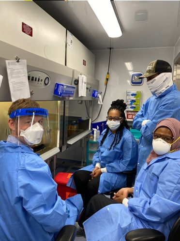 Laboratory staff wearing scrubs and other personal protective equipment pose for photo in lab.